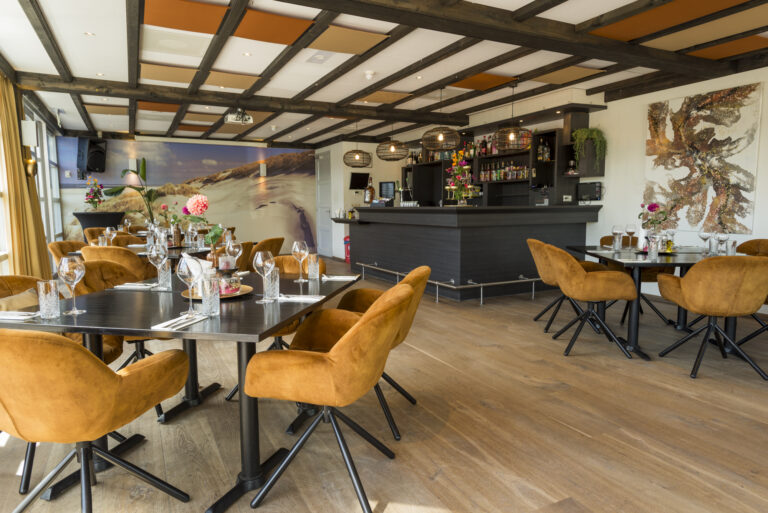 Sfeervol restaurant en bar met gedekte tafels, okergele stoelen en een muurschildering van zandduinen.