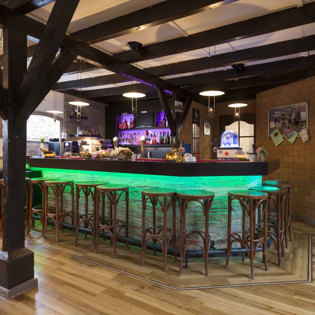 Bar in evenementenlocatie met groene LED-verlichting, houten krukken, donkere balken en feestelijke ballonnen.