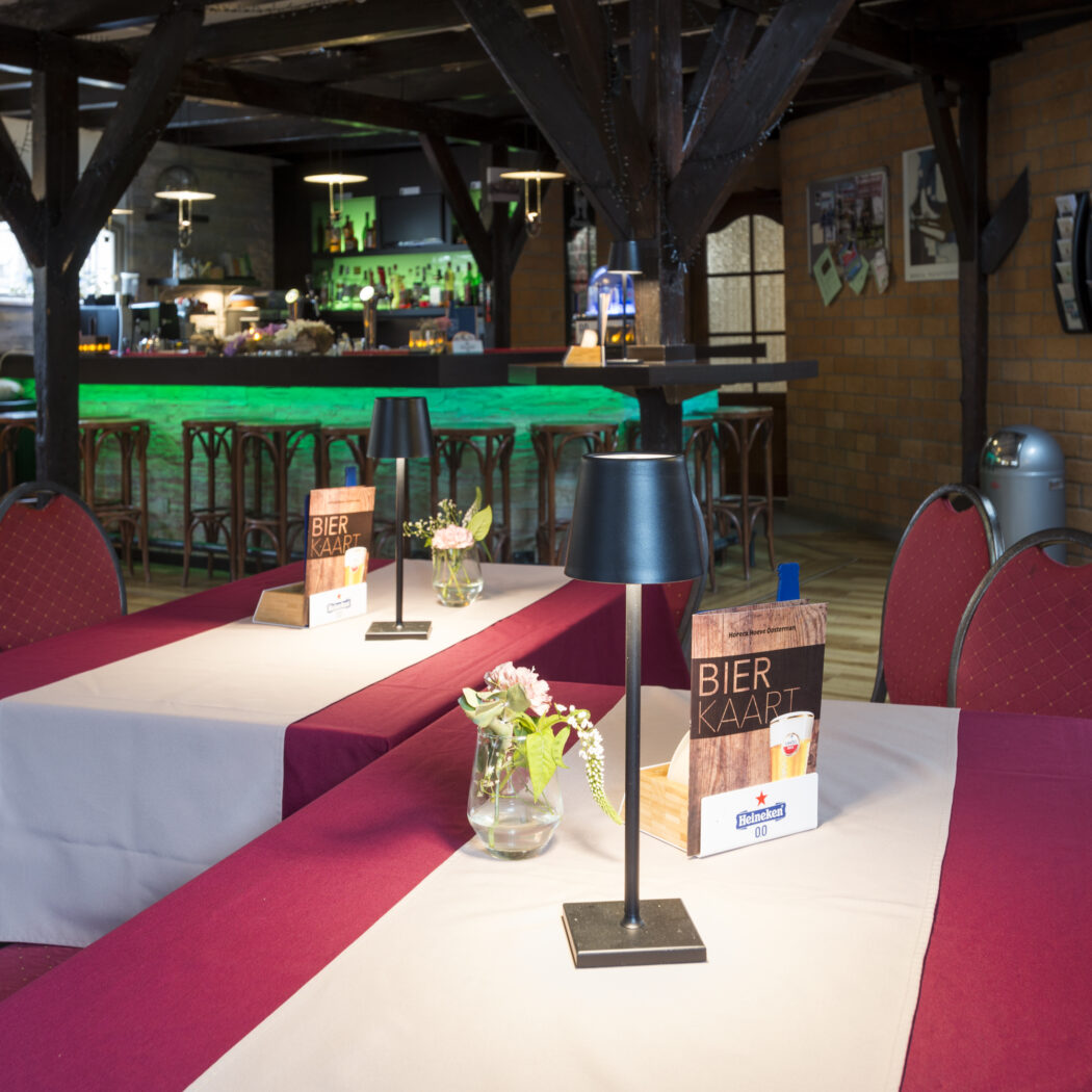 Sfeervol restaurant interieur met gedekte tafels, rode stoelen, Bier Kaart en een groene verlichte bar.