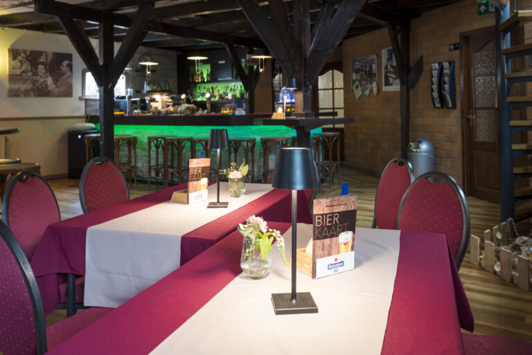 Sfeervol restaurant interieur met gedekte tafels, rode stoelen, Bier Kaart en een groene verlichte bar.