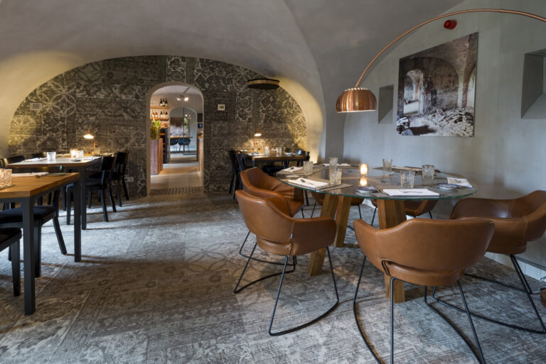 Modern restaurant met gewelfde, gedecoreerde muren, ronde glazen tafel, bruine lederen stoelen en koperen lamp.