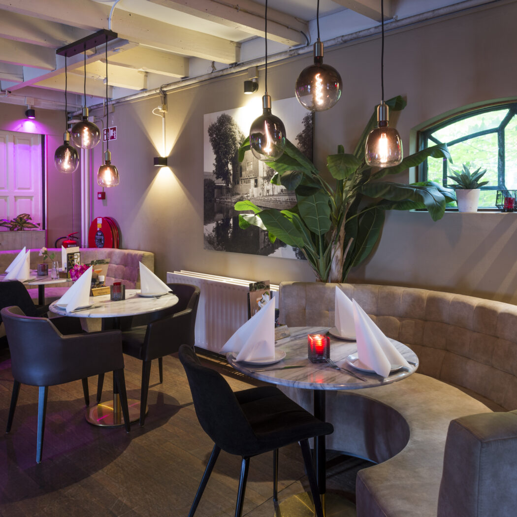 Gezellig restaurant met ronde marmeren tafels, comfortabele banken en sfeervolle verlichting.