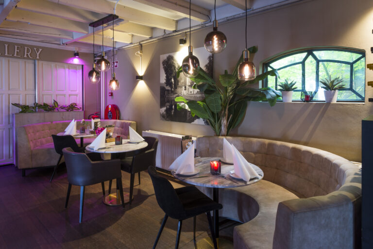 Gezellig restaurant met ronde marmeren tafels, comfortabele banken en sfeervolle verlichting.