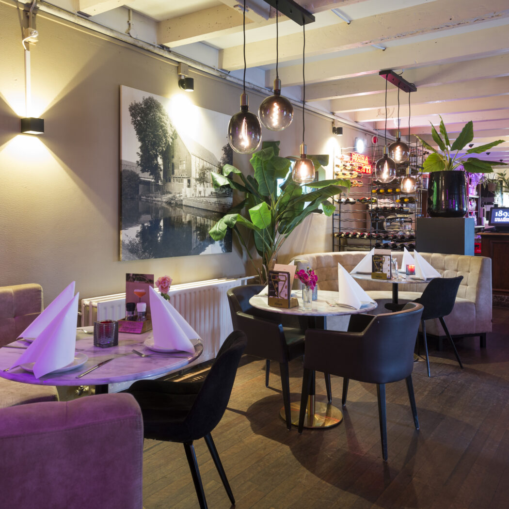 Modern restaurant interieur met marmeren tafels, zachte banken, hanglampen en een bar met wijnrekken.