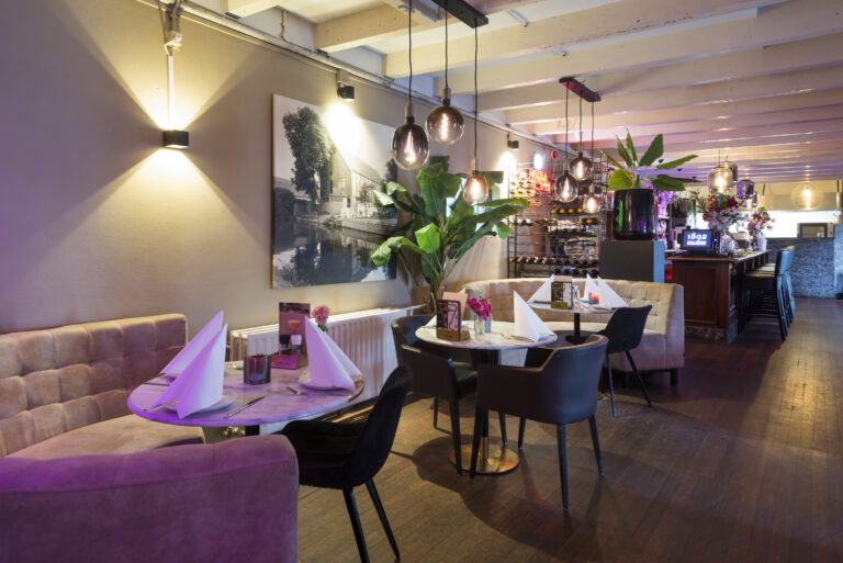 Modern restaurant interieur met marmeren tafels, zachte banken, hanglampen en een bar met wijnrekken.