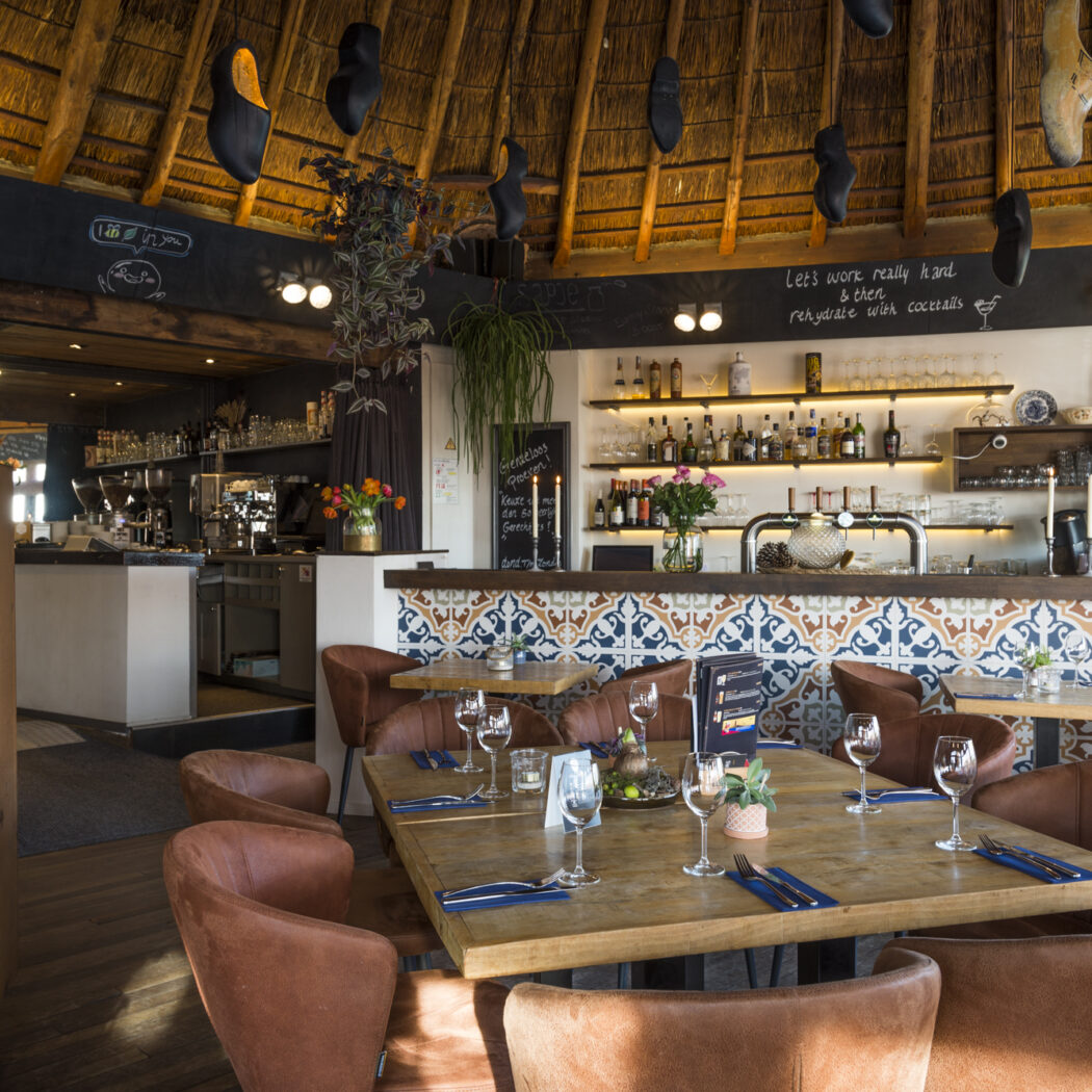 Sfeervol restaurant met rieten dak, een bar met kleurrijke tegels, bruine leren stoelen en een brandende haard.