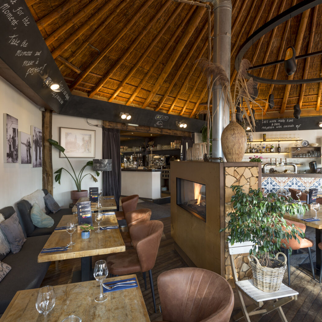 Sfeervol restaurant met rieten dak, houten tafels, leren stoelen, een brandende open haard en bar.