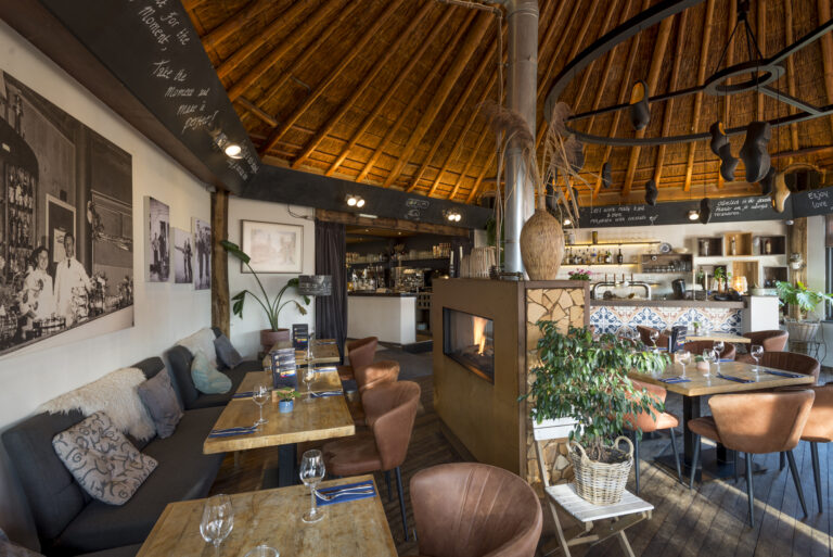 Sfeervol restaurant met rieten dak, houten tafels, leren stoelen, een brandende open haard en bar.