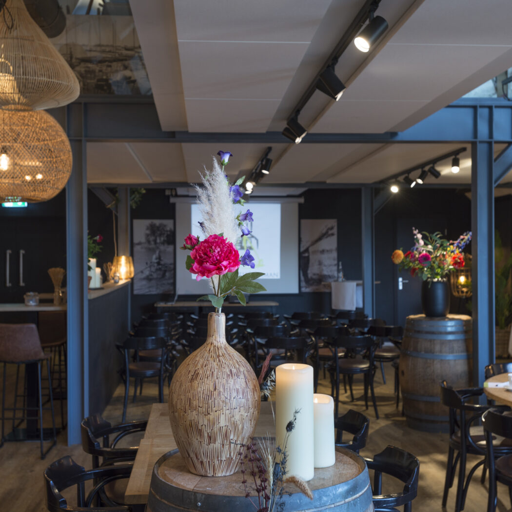 Sfeervolle evenementenruimte met bar, presentatiezaal en zitgedeeltes, versierd met rieten lampen, bloemen en kaarsen.