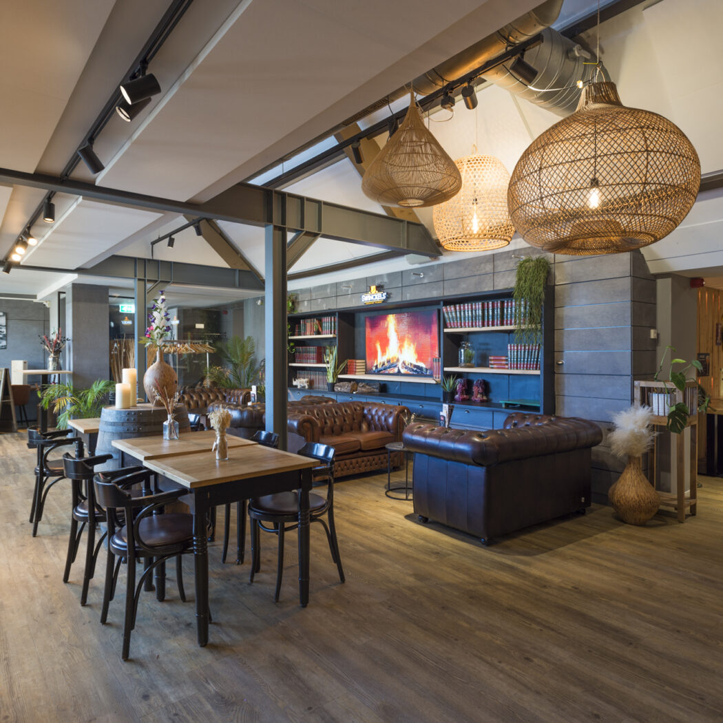 Sfeervol restaurant met leren banken, houten tafels, grote rieten hanglampen en een tv-scherm met haardvuur.