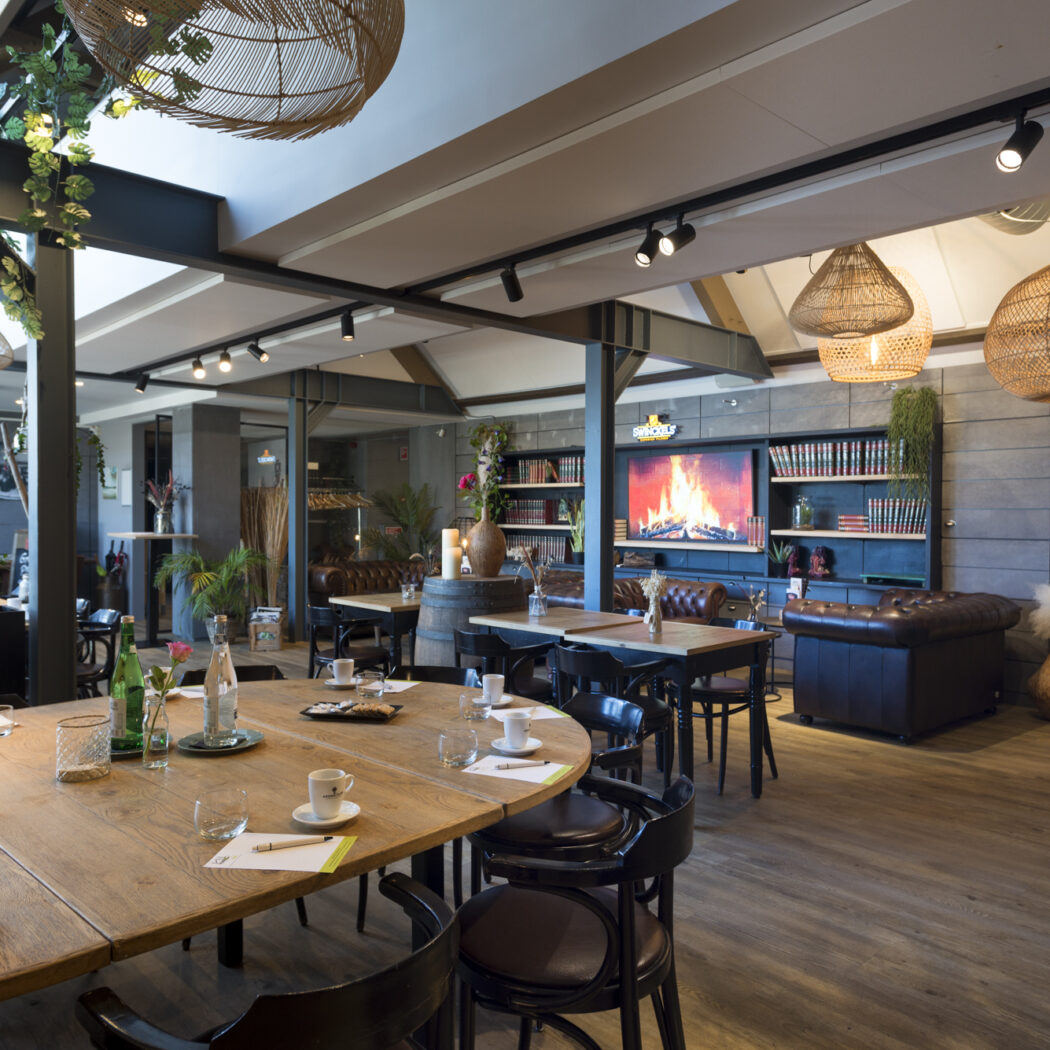 Sfeervol interieur met houten vergadertafel, rieten hanglampen en tv met haardvuur, inclusief SMOKEY-logo.