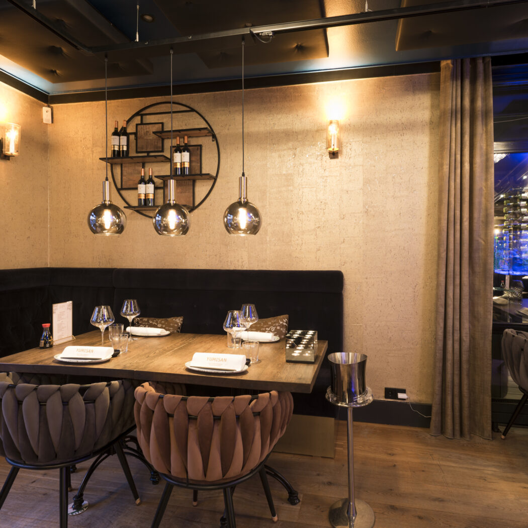 Modern restaurantinterieur met houten eettafel, bruine en roze gevlochten stoelen en YUMISAN op de servetten.