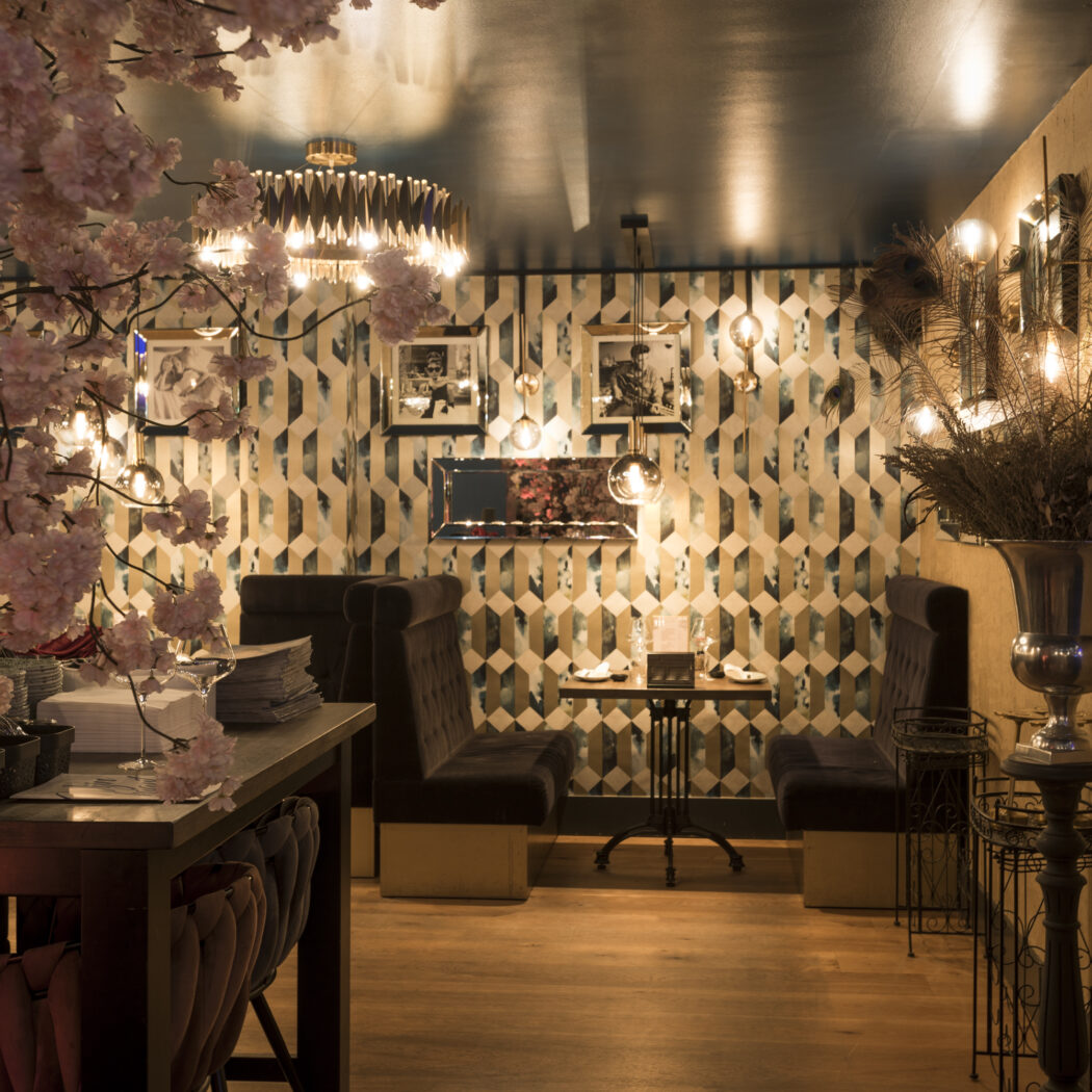 Sfeervol restaurantinterieur met roze kersenbloesem, donkere fluwelen zitbanken en geometrisch behang.