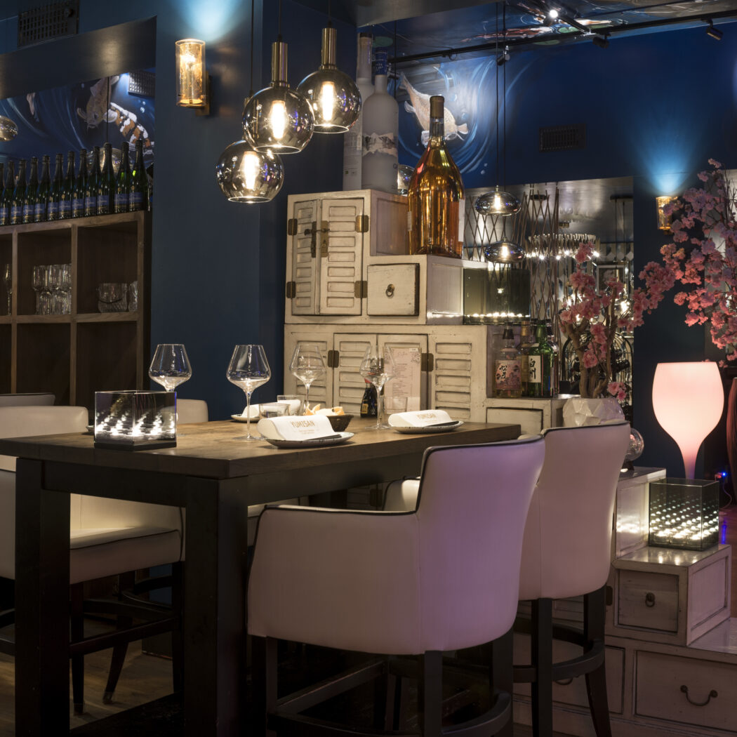 Stijlvol Japans restaurant met gedekte Yukio-San tafel, blauwe wand met koivissen en roze sfeerlicht.