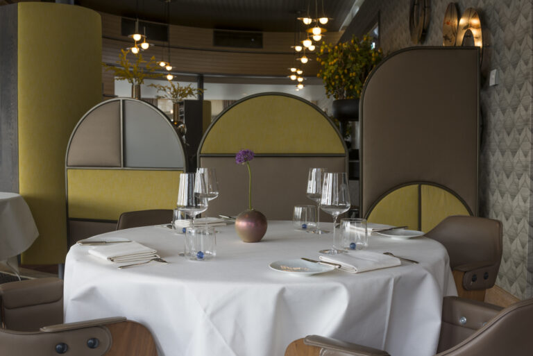 Elegant gedekte ronde restauranttafel met glazen, servies en een paarse bloem in een modern restaurantinterieur.
