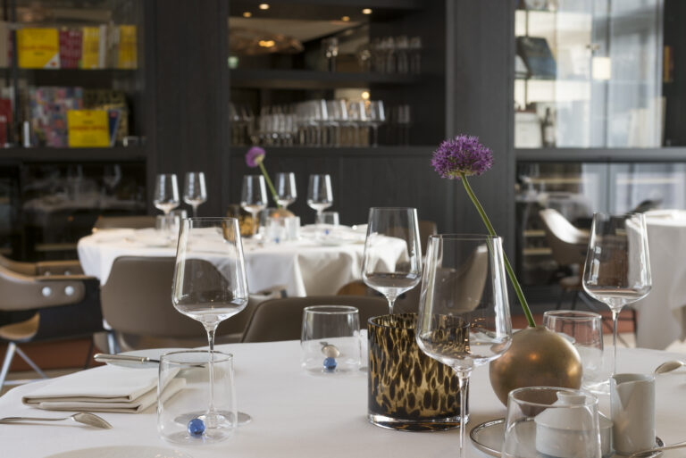 Gedekte restauranttafel met wijnglazen, bestek, paarse sierui en waterglazen met blauwe glazen bolletjes.