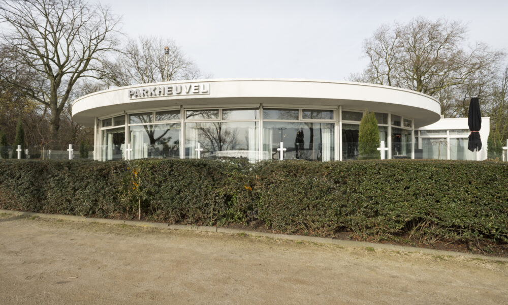 Modern wit gebouw PARKHEUVEL met rond dak en glazen gevel, omringd door kale bomen en een heg.