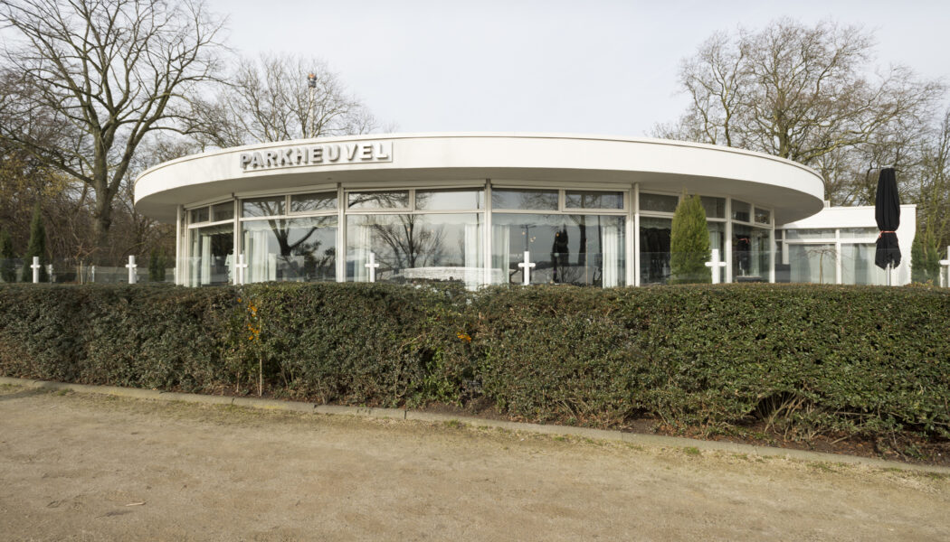 Modern wit gebouw PARKHEUVEL met rond dak en glazen gevel, omringd door kale bomen en een heg.