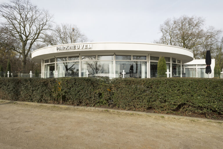 Modern wit gebouw PARKHEUVEL met rond dak en glazen gevel, omringd door kale bomen en een heg.