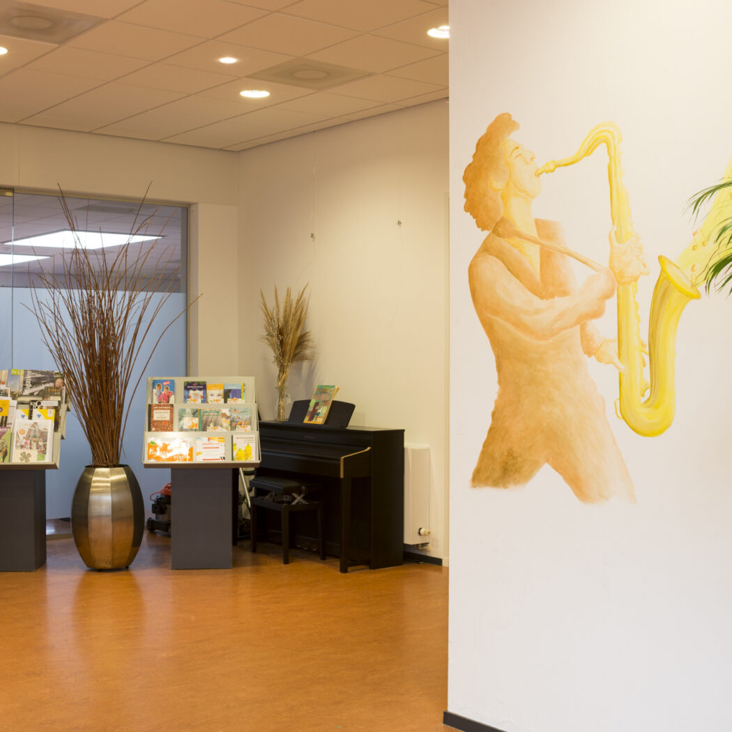 Lichte ontvangstruimte met grote muurschildering van saxofonist, folderdisplays en een zwarte piano.