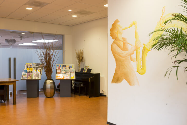 Lichte ontvangstruimte met grote muurschildering van saxofonist, folderdisplays en een zwarte piano.