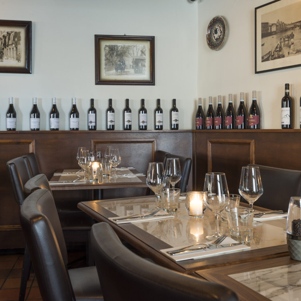 Gedekte tafels met kaarslicht en rijen wijnflessen in een sfeervol restaurantinterieur.