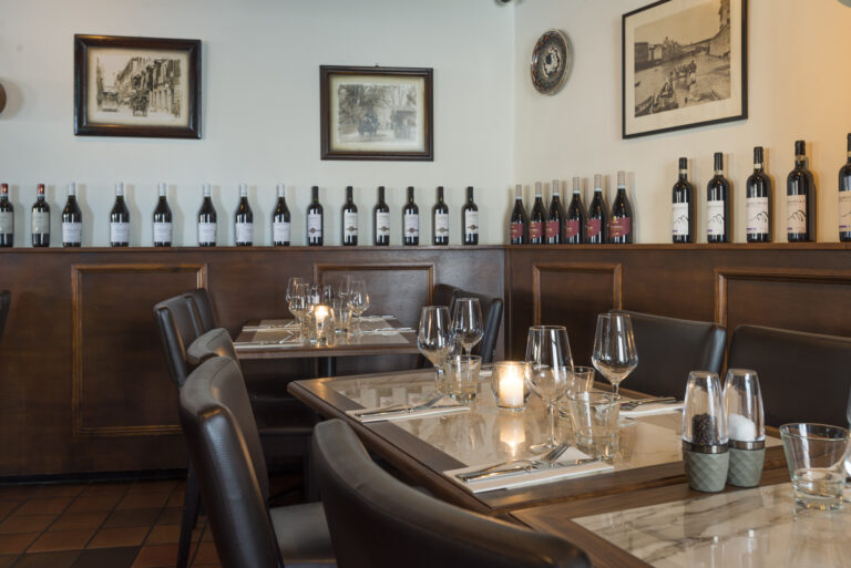 Gedekte tafels met kaarslicht en rijen wijnflessen in een sfeervol restaurantinterieur.