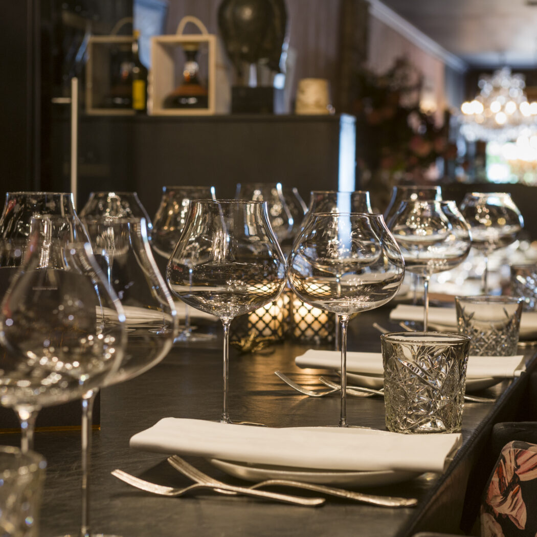 Elegant gedekte restauranttafel met glanzende wijnglazen, waterglazen, witte servetten en bestek.