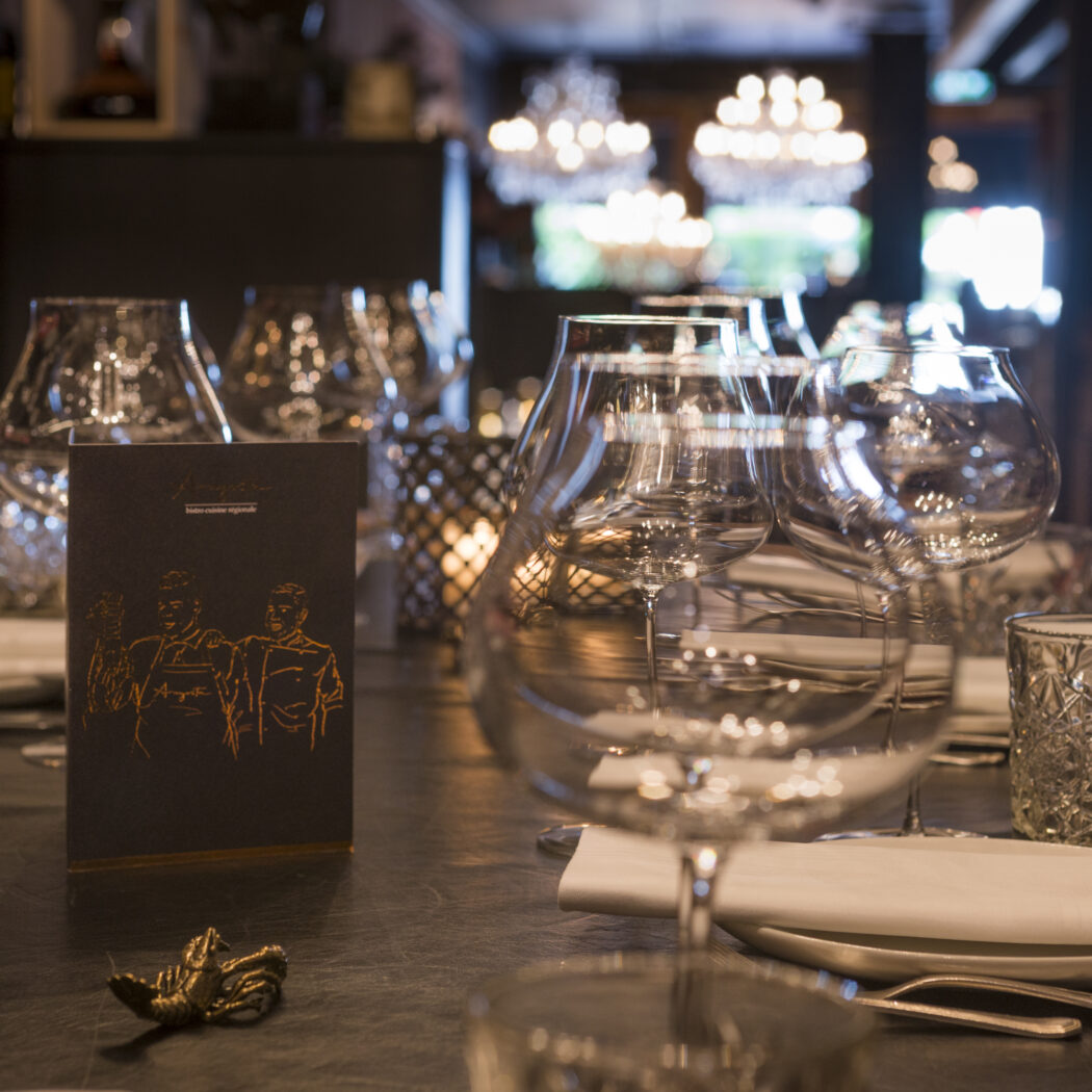 Een elegant gedekte restauranttafel met diverse glazen, een zwart Amice-menu, bestek en een gouden kreeft.