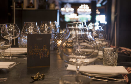 Dichtbij tafelschikking met glazen, menukaart en kreeftdecoratie; achtergrond onscherp met restaurantinterieur.