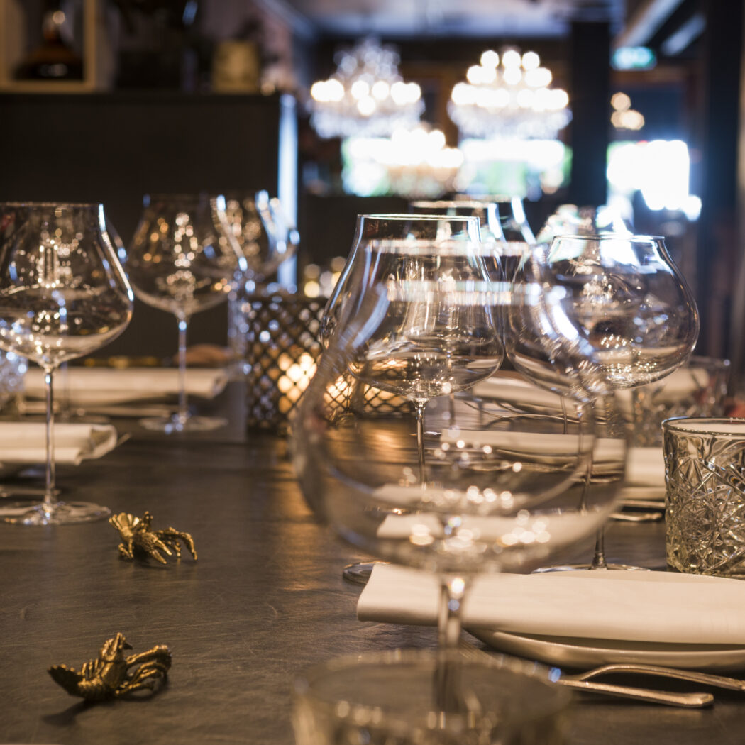 Elegant gedekte restauranttafel met diverse wijnglazen, witte servetten en sfeervolle verlichting.