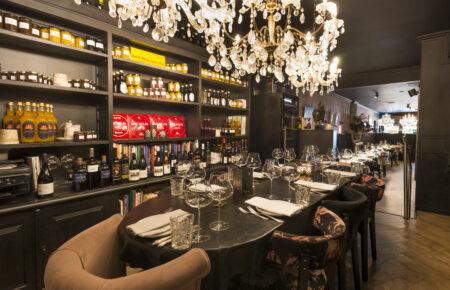 Restaurantinterieur: gedekte tafel, kristallen kroonluchter,  wijnrek en gevulde schappen.