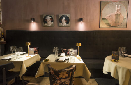 Restaurant interieur: gedekte tafels, bank, wand met schilderijen.