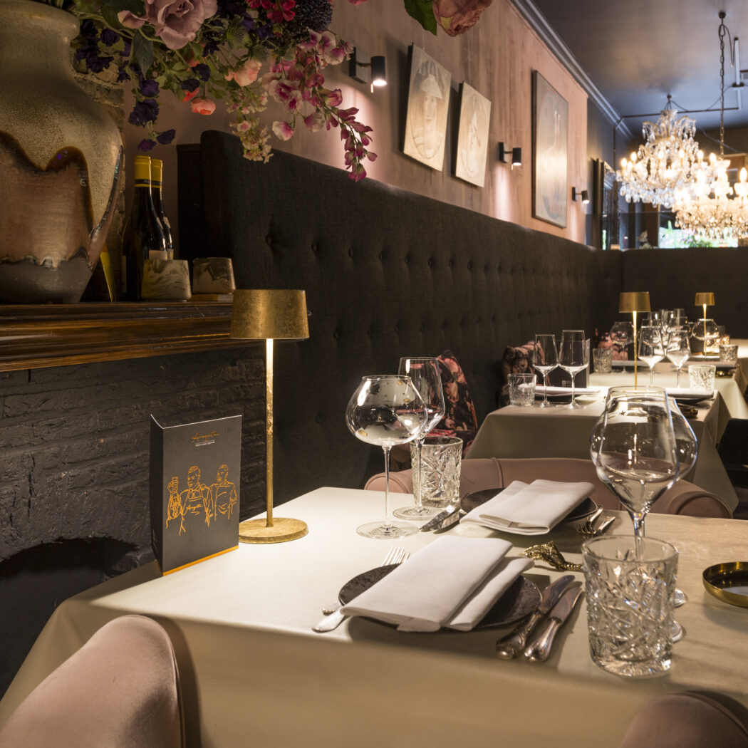 Luxe restaurantinterieur met gedekte tafels, donkere gestoffeerde banken en fonkelende kroonluchters.