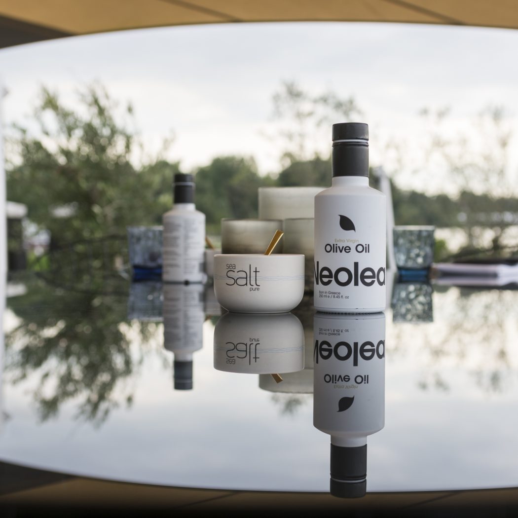 Witte Neoled olijfoliefles en bakje sea salt pure met gouden lepel op een reflecterende buitentafel.