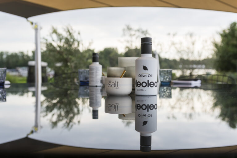Witte Neoled olijfoliefles en bakje sea salt pure met gouden lepel op een reflecterende buitentafel.