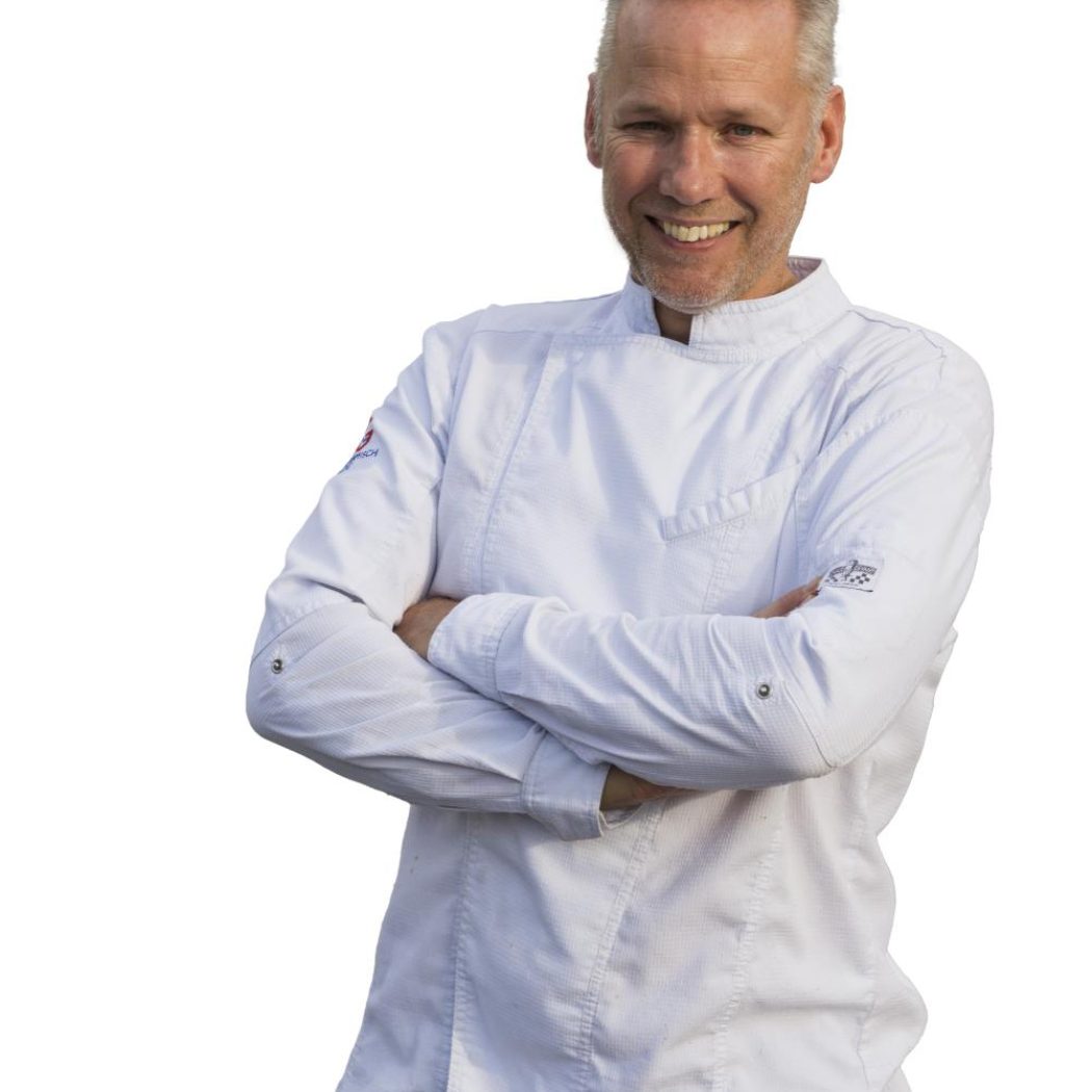 Lachende chef-kok in witte koksbuis met gekruiste armen.