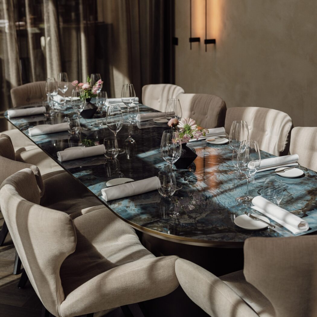 Lange, elegant gedekte dinertafel met blauw marmeren blad, beige stoelen en roze bloemstukken.