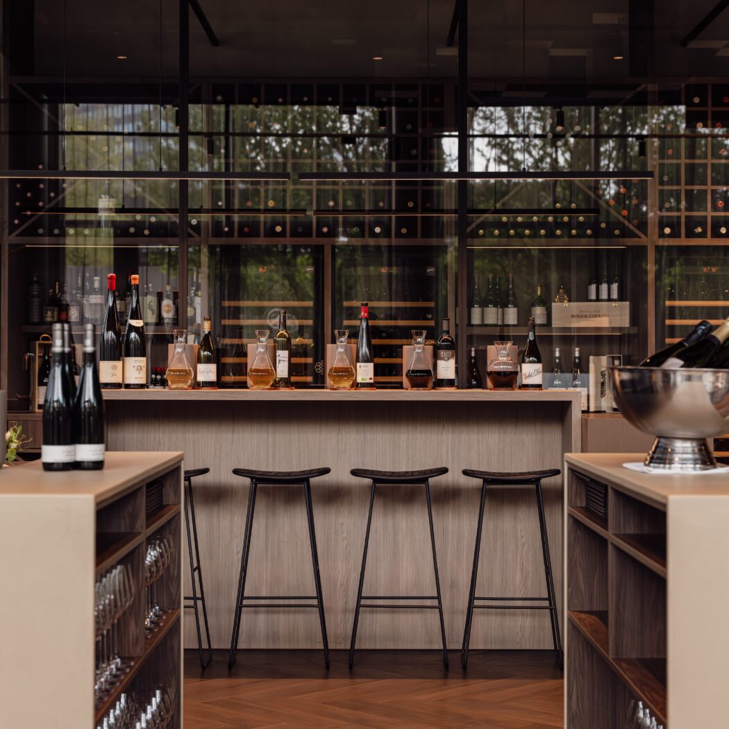 Sfeervol interieur van een moderne wijnbar met diverse wijnen op de balie, barkrukken en grote wijnrekken.