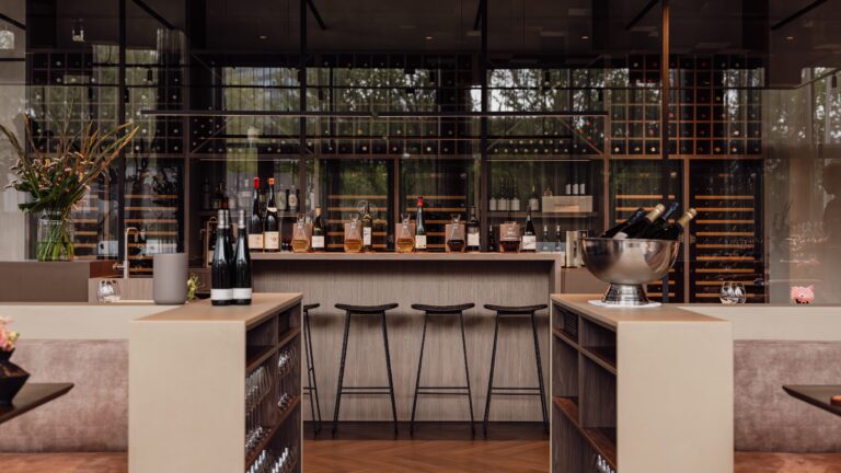 Sfeervol interieur van een moderne wijnbar met diverse wijnen op de balie, barkrukken en grote wijnrekken.