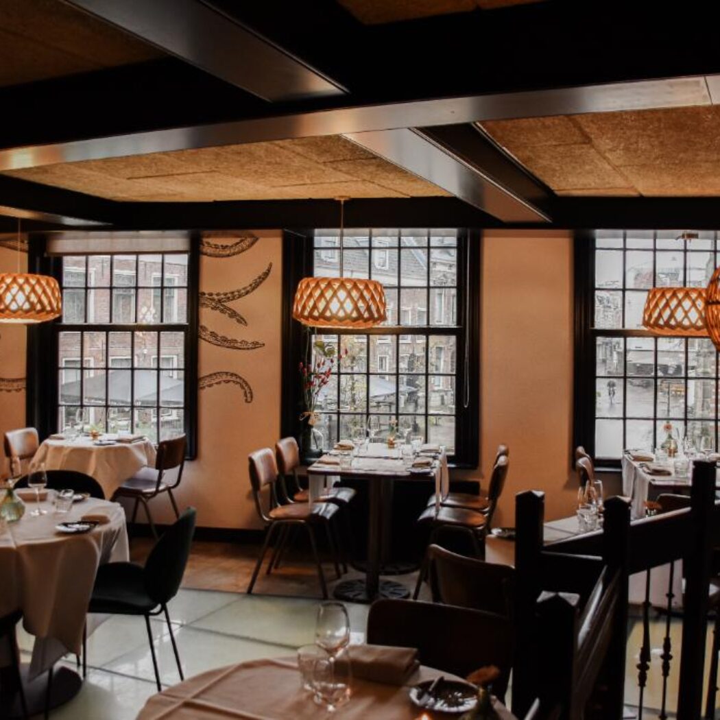 Sfeervol restaurantinterieur met gedekte tafels, grote ramen en een opvallende octopusmuurschildering.
