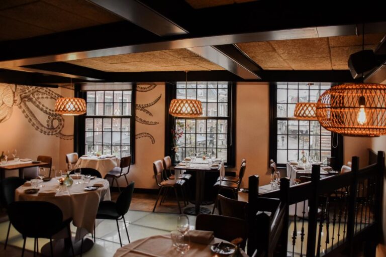 Sfeervol restaurantinterieur met gedekte tafels, grote ramen en een opvallende octopusmuurschildering.