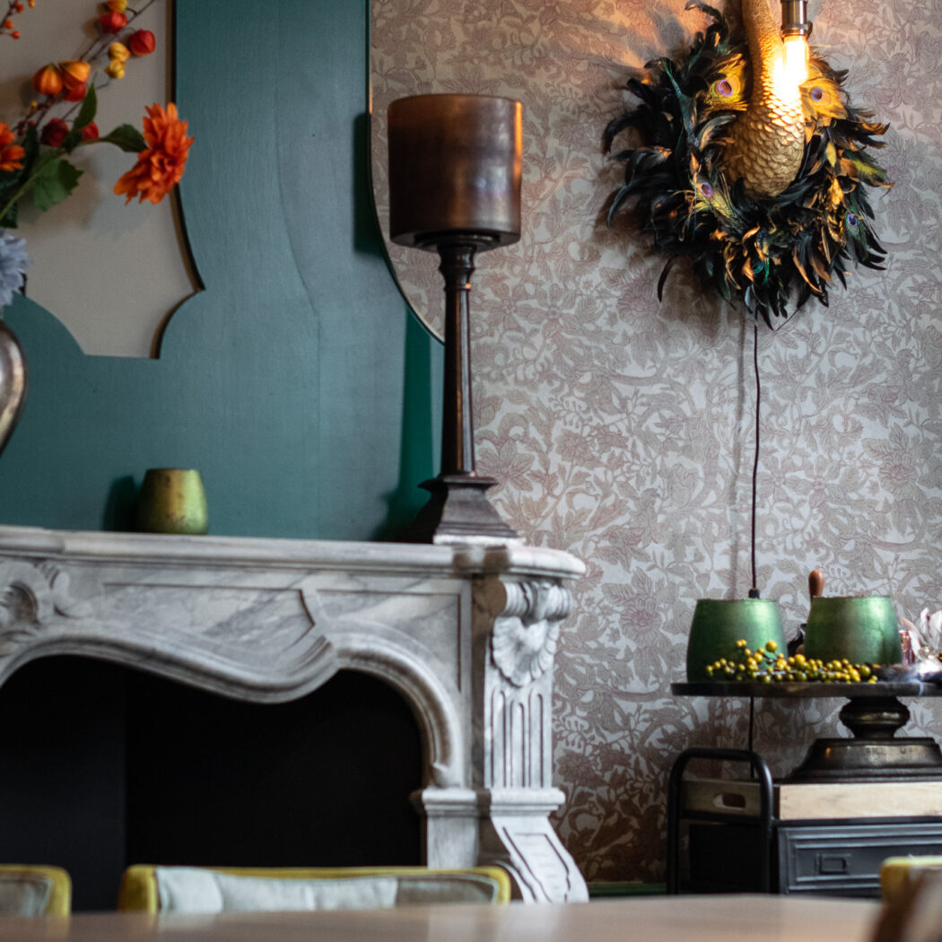 Stijlvolle kamer met geornamenteerde marmeren schouw, verlichte pauw wandlamp met veren en gedessineerd behang.