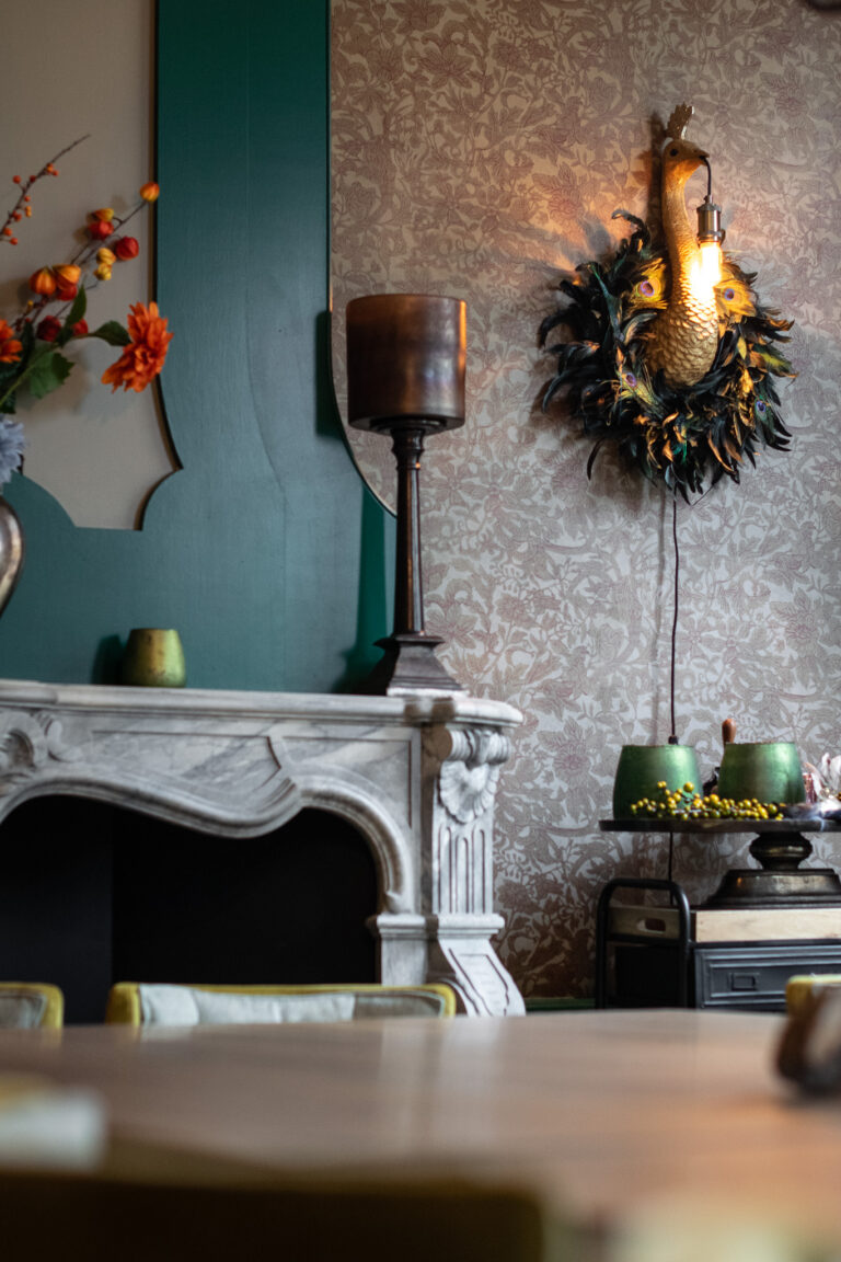 Stijlvolle kamer met geornamenteerde marmeren schouw, verlichte pauw wandlamp met veren en gedessineerd behang.