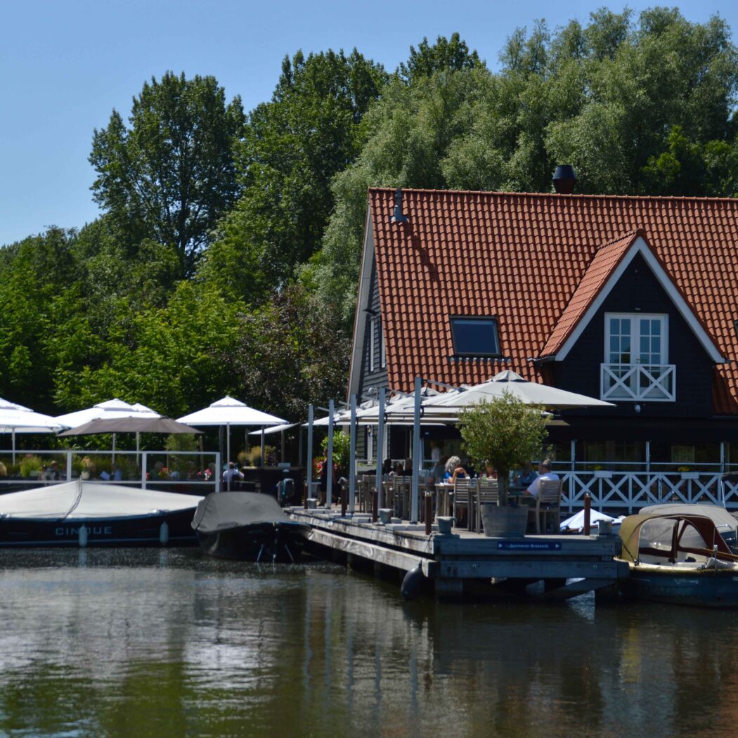 Waterfront restaurant met rood pannendak, een druk terras met etende gasten en aangemeerde boten.