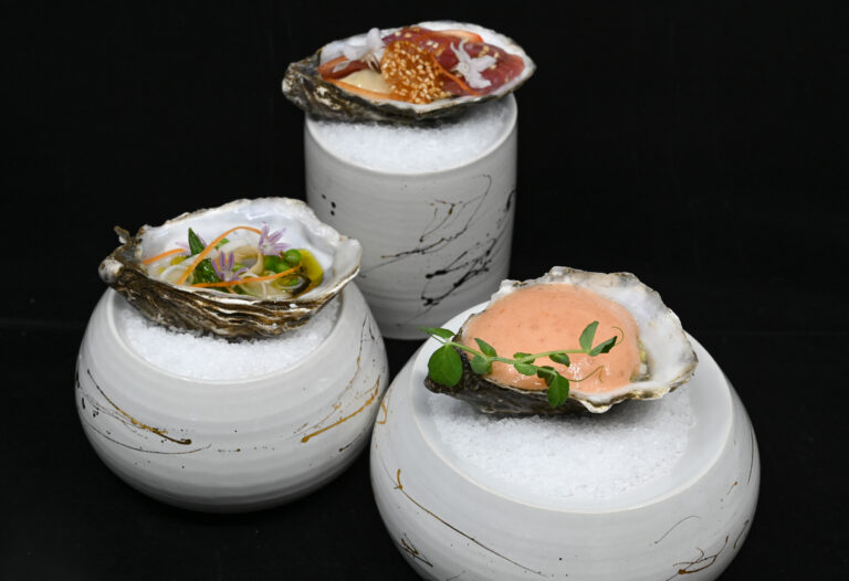 Drie luxe oestergerechten op ijs, geserveerd in decoratieve witte schaaltjes met abstracte spetters.
