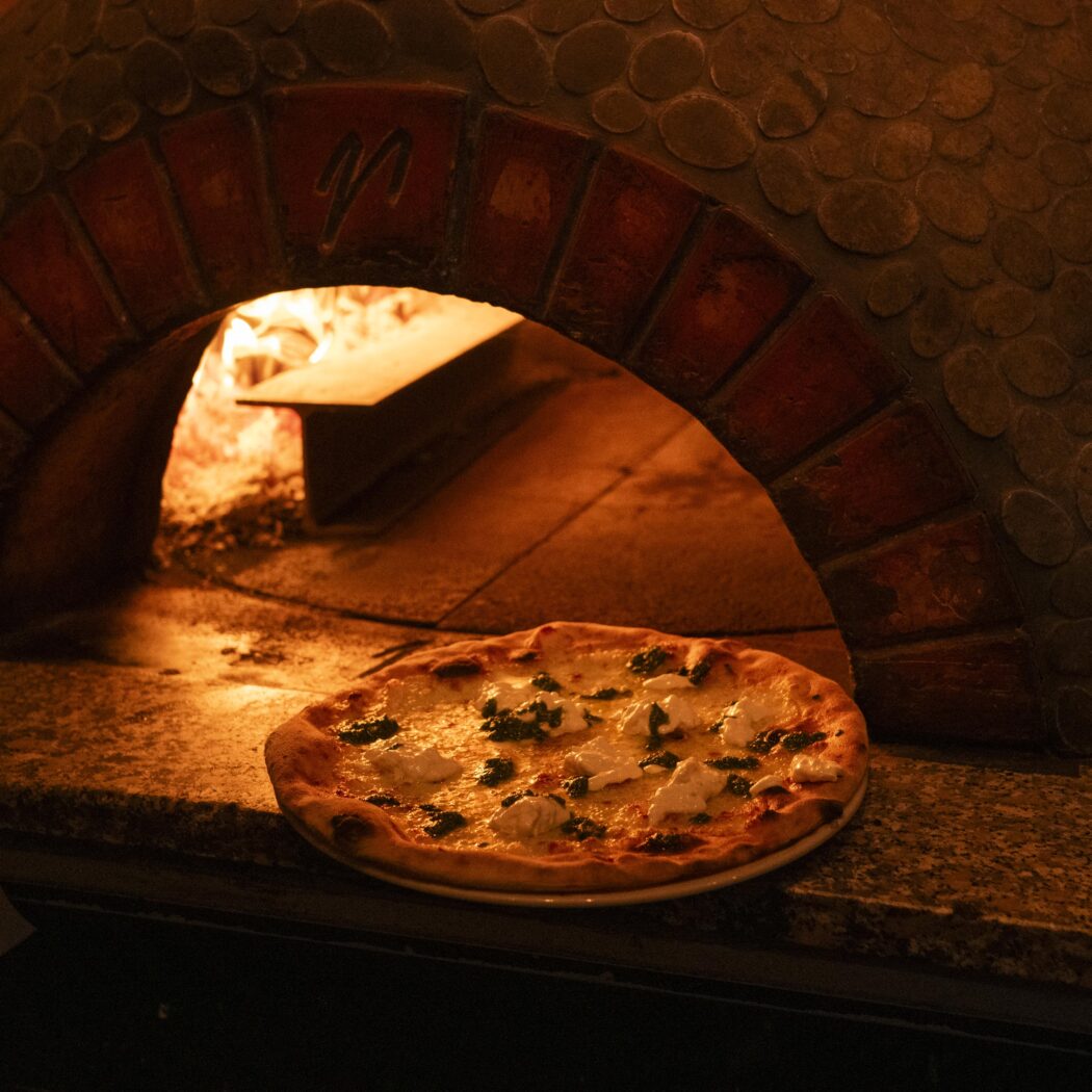 Vers gebakken pizza met ricotta en groene kruiden voor een gloeiende, stenen pizzaoven.