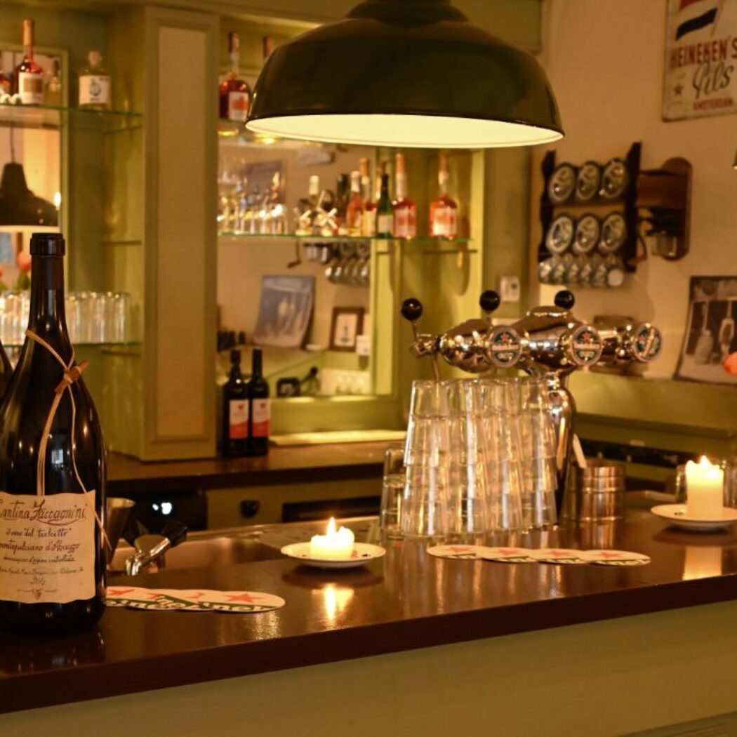 Warme barinterieur met Cantina Zaccagnini wijnflessen, brandende kaarsen, biertaps en Heineken details op de houten toonbank.