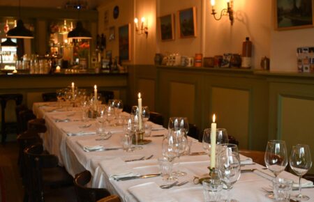 Feestelijk gedekte lange eettafel met brandende kaarsen en glazen in een sfeervol restaurant.