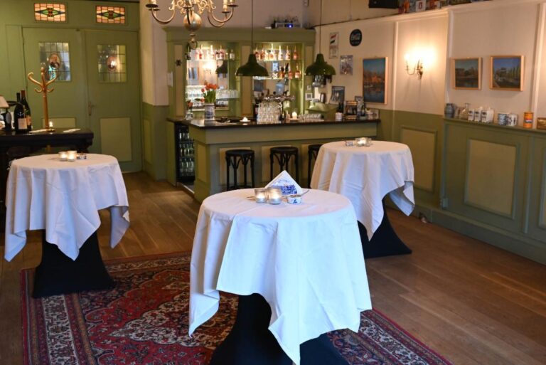 Sfeervolle barruimte met witte sta-tafels, een groene houten bar en rood tapijt op een houten vloer.